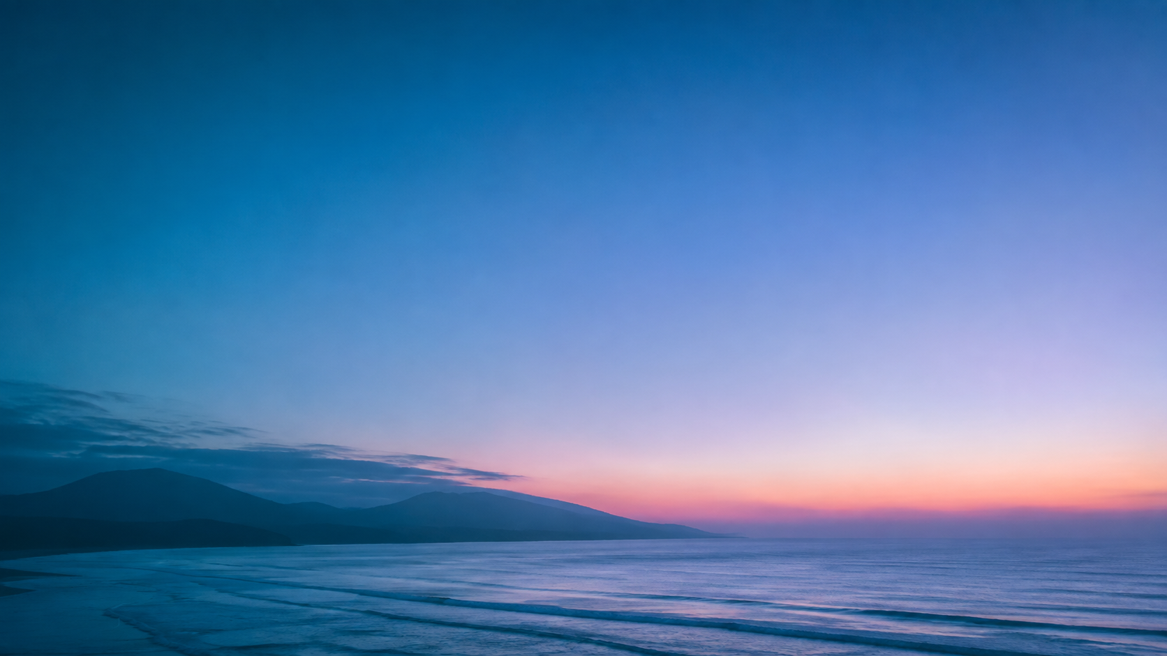 Horizonte costero al atardecer con cerros al fondo y oleaje suave